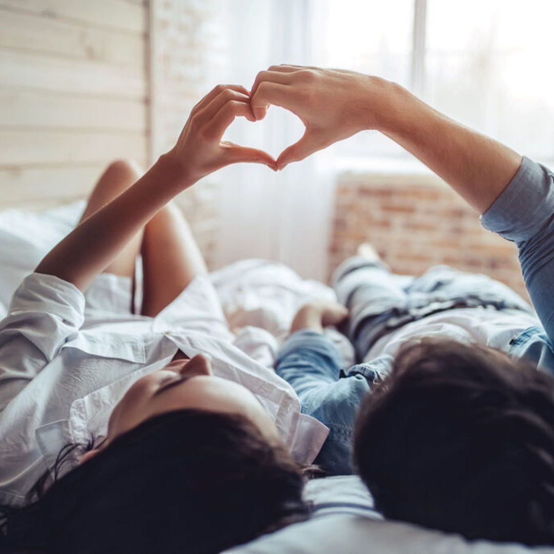 Two people laying in bed holding hands together to form a heart