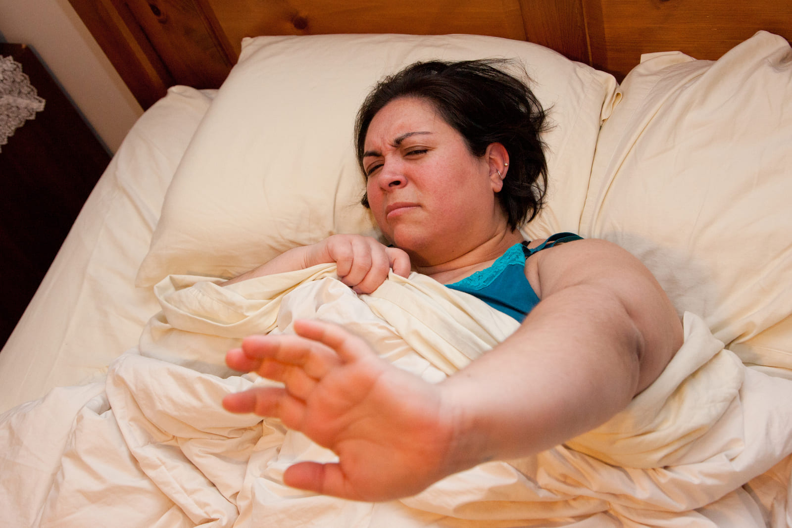 Cranky woman waking up in bed with her hand out trying to block the camera